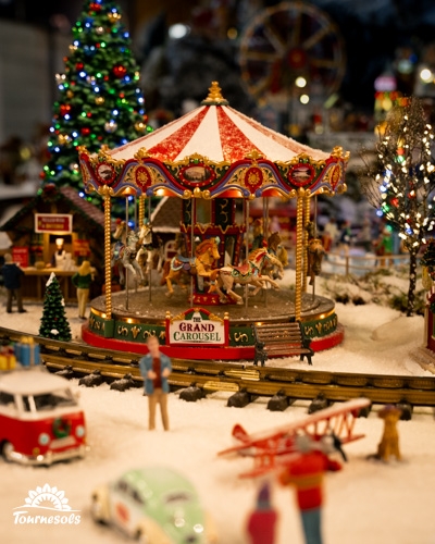 Carrousel miniature rouge et blanc d'un village de Noël enneigé, entouré de figurines, d'un sapin et d'un petit train